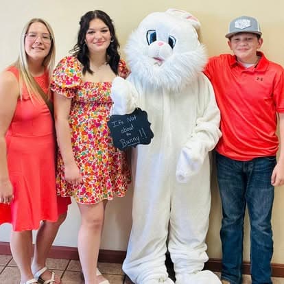Three people pose with the Easter Bunny holding a sign: It's Not about the Bunny.