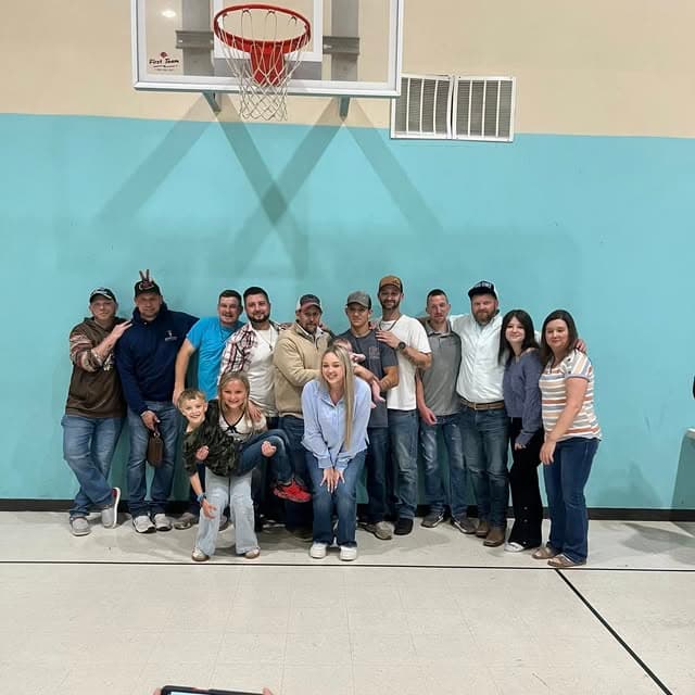 A large group of people posing together in a gymnasium under a basketball hoop.