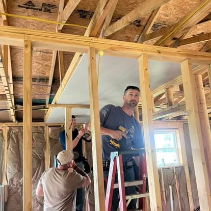 Construction workers use power drills to install drywall onto wooden framing in a new building.